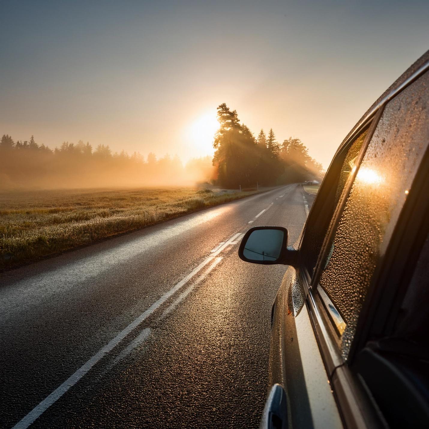 A car on a road with the sun shining through.
